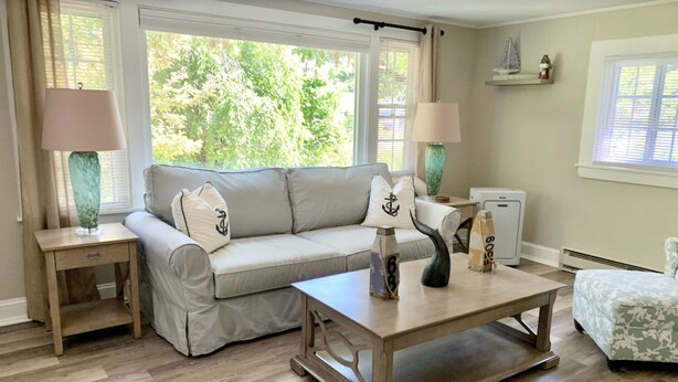 A living room with a beige sofa, two side tables with lamps, a coffee table, and a view of greenery outside.