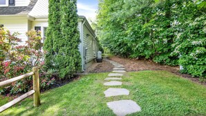 A pathway leading to a house surrounded by lush greenery and a wooden fence.