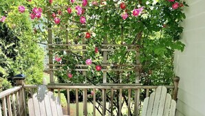 A wooden deck with two Adirondack chairs and a wooden trellis with pink flowers.