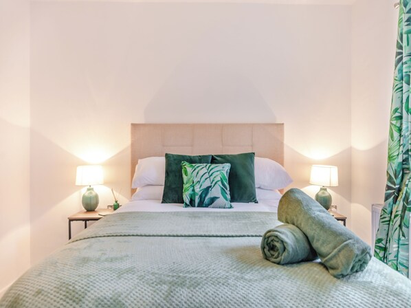 Un letto ben rifatto con un cuscino verde e bianco, due lampade da comodino e un asciugamano arrotolato sul letto.