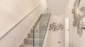 Uma escadaria com guarda-corpo de vidro, um enfeite de árvore fixado na parede e um radiador.
