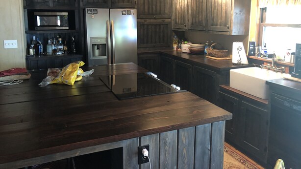 A kitchen with dark wooden cabinets, a stainless steel refrigerator, a microwave, and a water dispenser. There is a wooden island with a sink and a bag of chips on it. - Private lakefront getaway with a sandy beach below the back deck! (Checotah)