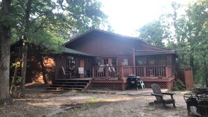 A rustic cabin with a wooden deck, surrounded by trees. - Private lakefront getaway with a sandy beach below the back deck! (Checotah)