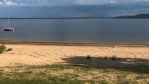 A beach with a boat, clear skies, and distant hills. - Private lakefront getaway with a sandy beach below the back deck! (Checotah)