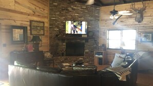 A cozy cabin interior with a stone fireplace, leather sofa, and a mounted deer head. - Private lakefront getaway with a sandy beach below the back deck! (Checotah)