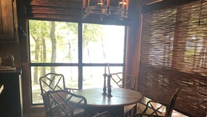 A dining area with a round table, six chairs, a chandelier, and a large window with blinds. - Private lakefront getaway with a sandy beach below the back deck! (Checotah)