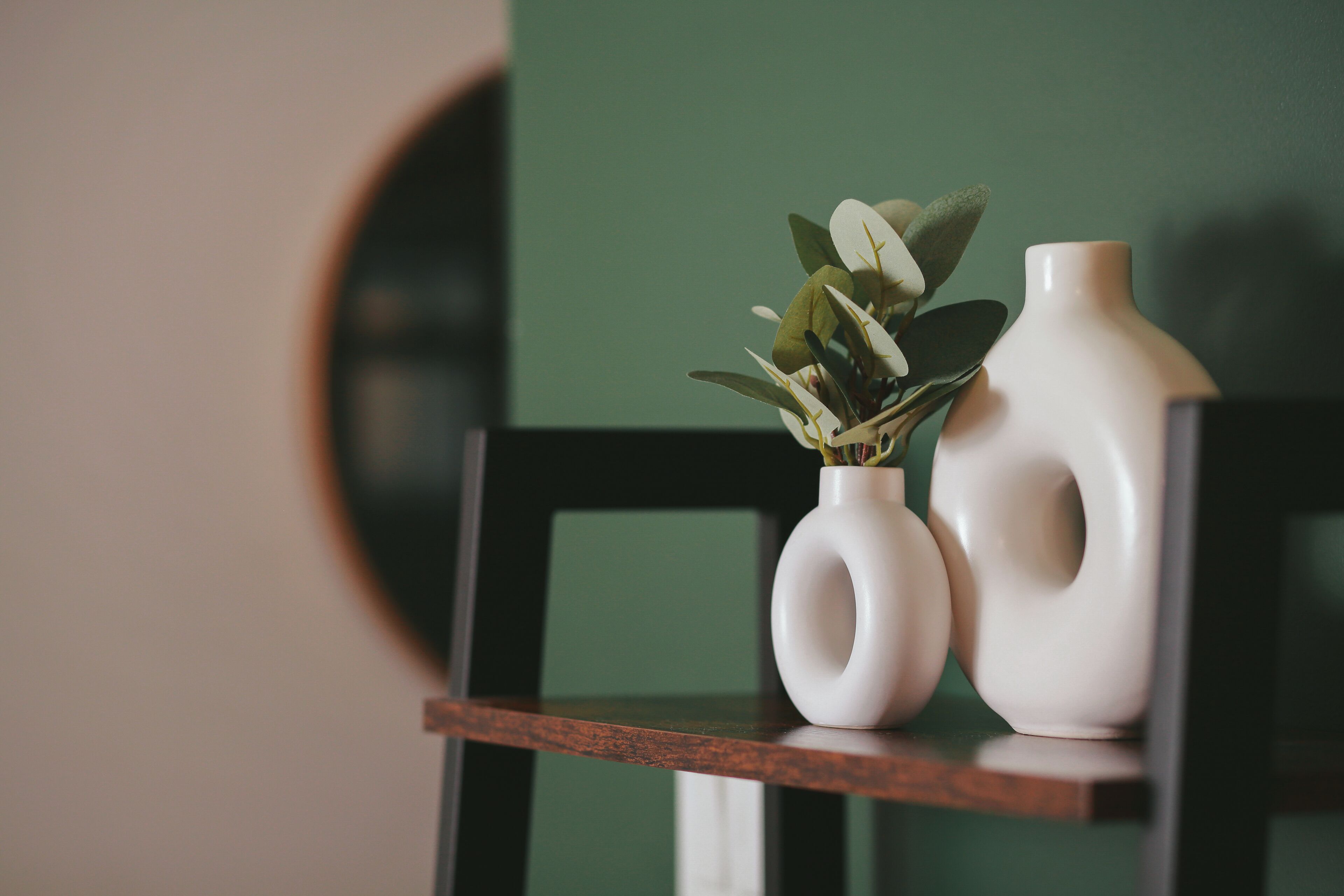 Two white vases with plants on a wooden shelf against a green wall.