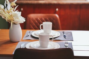 A dining table with white plates, a white cup, and a vase with white flowers.