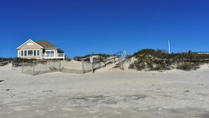 Une maison de plage dotée d’une terrasse clôturée et d’un escalier menant à la plage.
