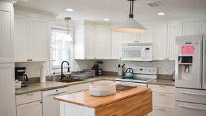 Une cuisine moderne avec des meubles blancs, un îlot central en bois, un four à micro-ondes encastré et un réfrigérateur en acier inoxydable.
