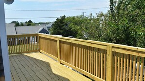Une terrasse en bois avec une rambarde, entourée de verdure et avec des maisons en arrière-plan.