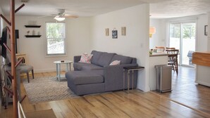 Un salon moderne avec un canapé d’angle gris, une petite table ronde et un plancher en bois.