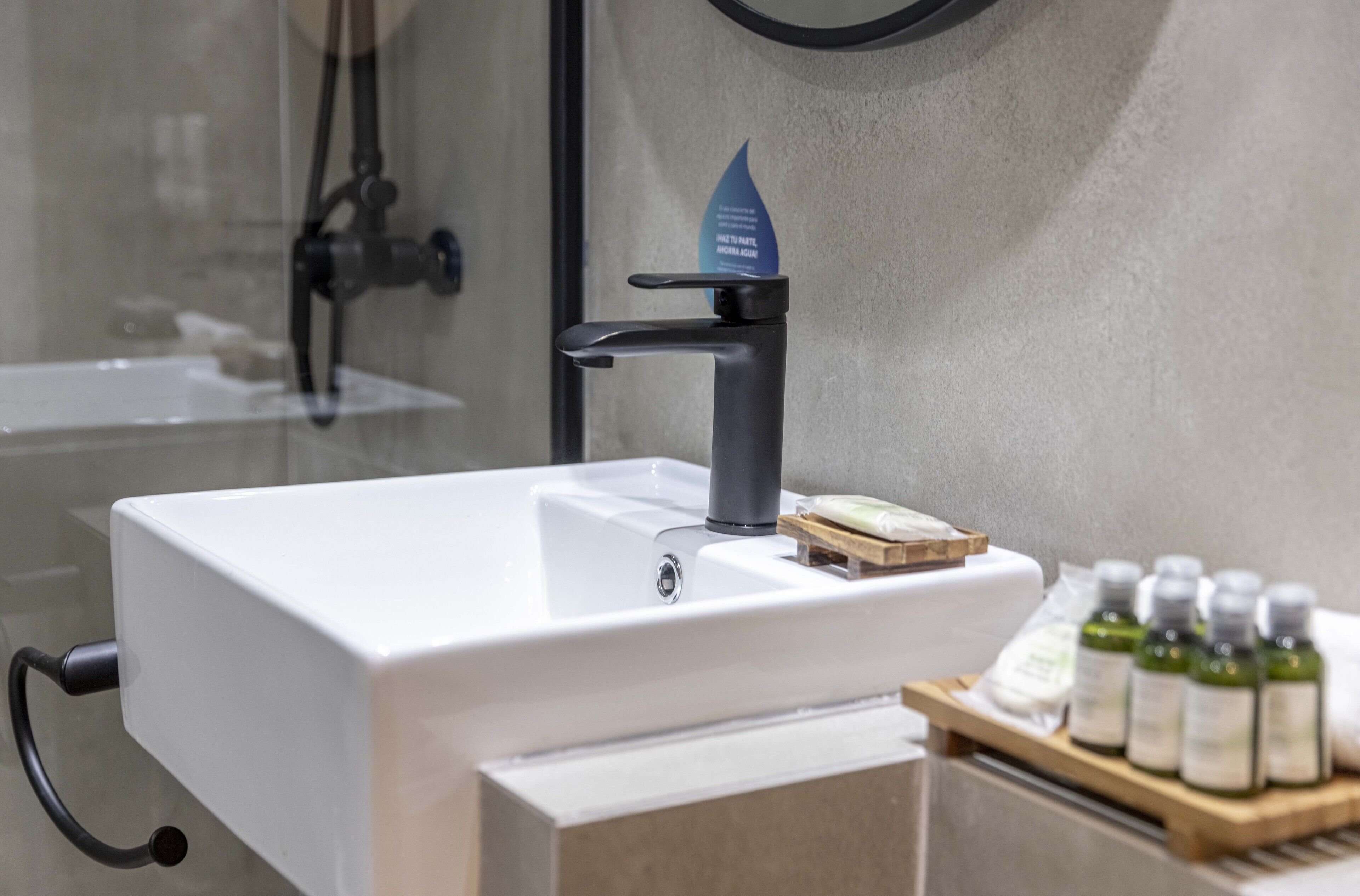 A bathroom with a white sink, a black faucet, and a wooden tray with bottles.