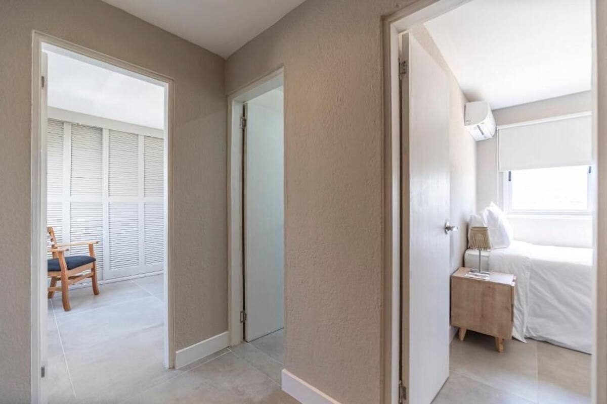 A bedroom with a bed, bedside table, and a chair in a hallway.