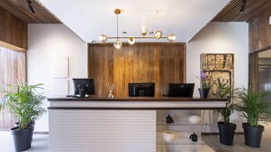 A reception desk with a wooden panel backdrop, a modern chandelier, and potted plants. - Hotel Montoya (Punta del Este)