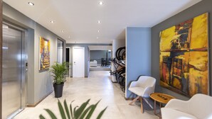 A modern hotel corridor with a potted plant, white chairs, and a large abstract painting on the wall. - Hotel Montoya (Punta del Este)