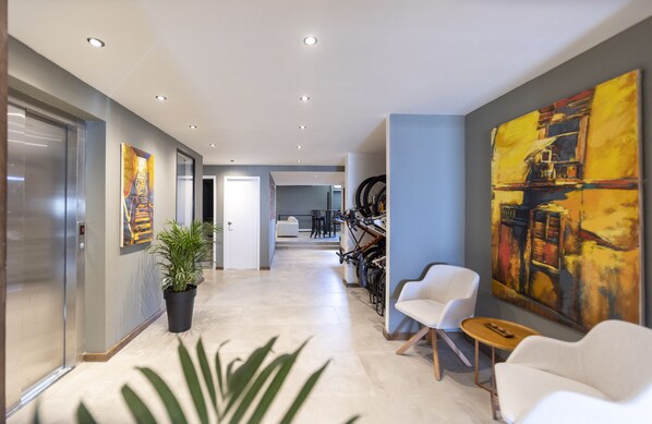 A modern hotel corridor with a potted plant, white chairs, and a large abstract painting on the wall. - Hotel Montoya (Punta del Este)