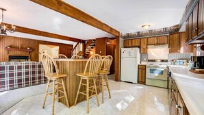 Une cuisine avec des meubles de rangement en bois, un îlot central doté de chaises, un réfrigérateur et une cuisinière.