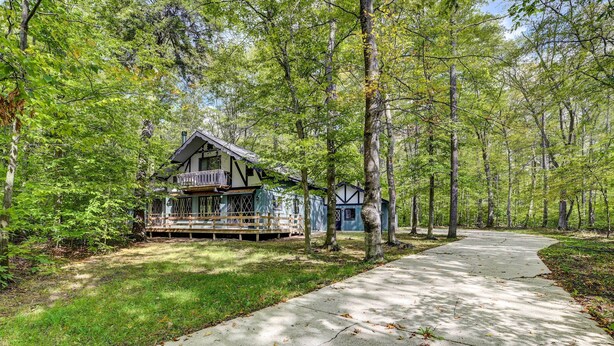 Une cabane dotée d’un porche, entourée d’arbres et bordée d’un chemin en béton.