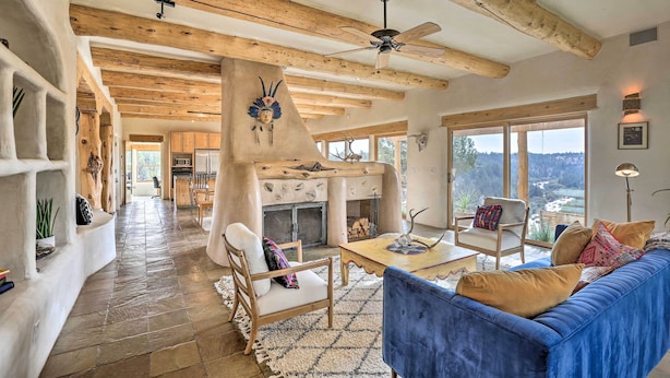 A spacious living area with a stone floor, wooden beams, a blue sofa, and a fireplace. - Adobe Home - River & Mtn Views w/ Hot Tub! (Redmond)