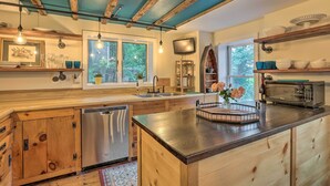 Una cocina moderna con armarios de madera, lavavajillas de acero inoxidable, una isla grande y un microondas. Hay ventanas con vistas a la vegetación exterior.
