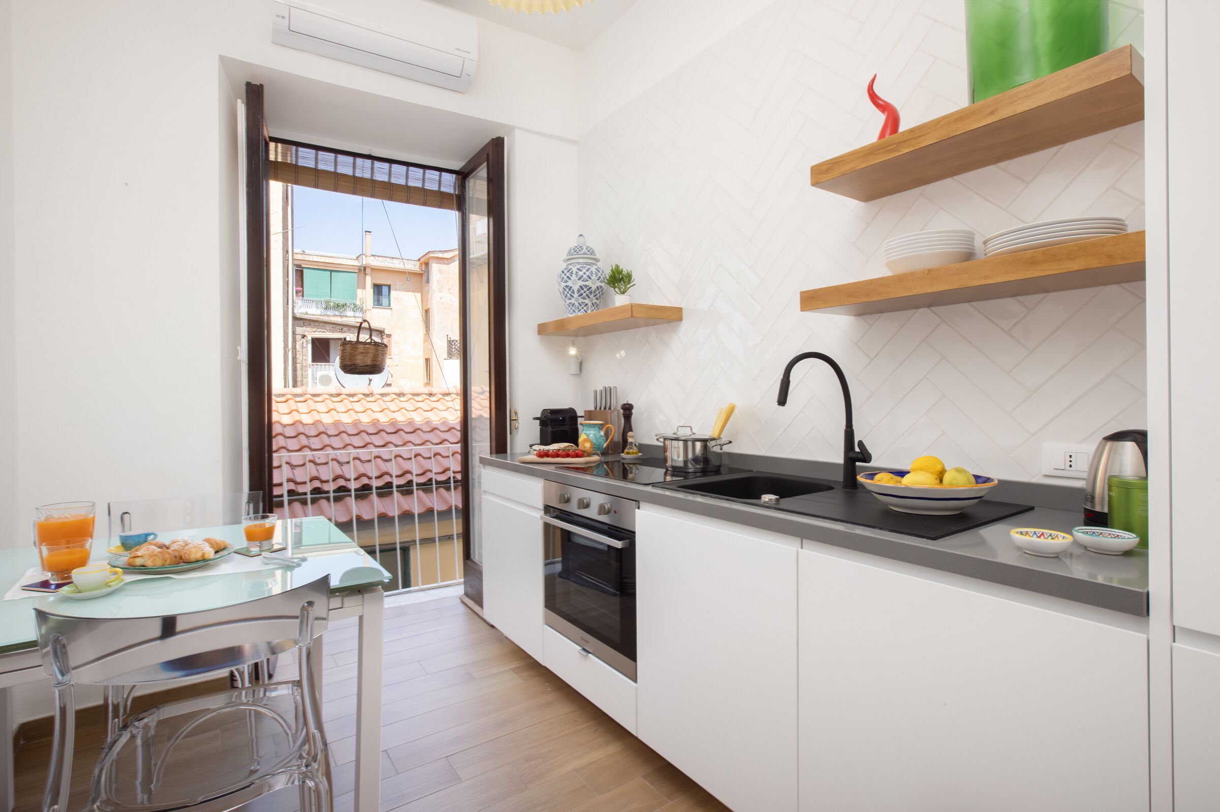 Une cuisine moderne avec des meubles blancs, un évier noir et une table en verre sur laquelle sont disposés des aliments pour le petit-déjeuner.