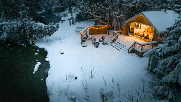 Un paysage enneigé avec un chalet doté d’une terrasse, de meubles d’extérieur et de guirlandes lumineuses.