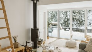 Un salon chaleureux avec une grande fenêtre, un poêle à bois noir et un coin salon confortable.