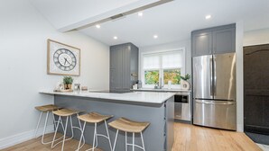 Une cuisine moderne avec des meubles gris, un réfrigérateur en acier inoxydable et un grand îlot central doté de tabourets de bar.