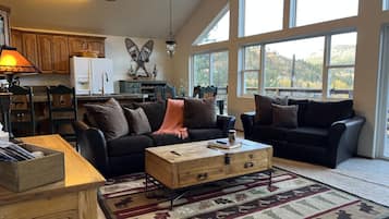 Ein geräumiges Wohnzimmer mit zwei Sofas, einem Holztisch und einem großen Fenster mit Blick ins Freie.