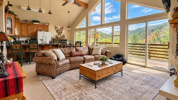 A spacious living room with a large sectional sofa, a coffee table, and a view of a mountainous landscape through large windows.