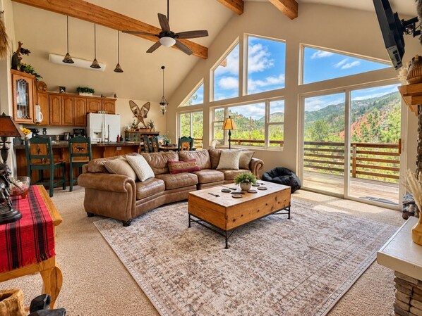 A spacious living room with a large sectional sofa, a coffee table, and a view of a mountainous landscape through large windows.