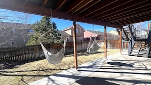 A covered patio area with two hammocks hanging from wooden beams, a concrete floor, and a wooden fence in the background. - Spacious 6-BDR Near USAFA with Mountain Views *Pet Friendly* (Colorado Springs)