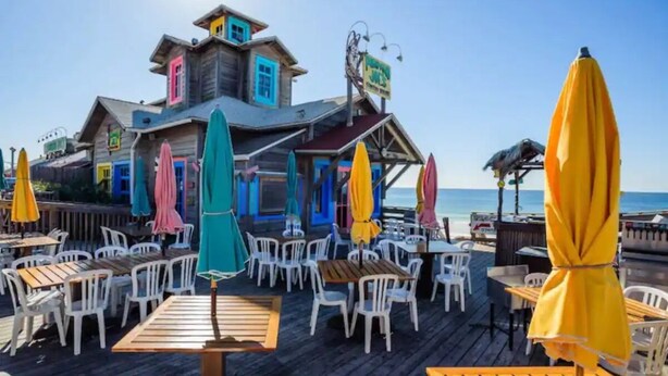 Une terrasse en bois avec des sièges et des parasols, donnant sur une plage.
