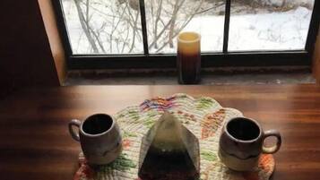 A window with a view of a snowy landscape, a wooden table with a placemat, and two ceramic mugs.