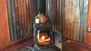 Ein Kaminofen mit Schornstein vor einer wellenförmigen Metallwand.