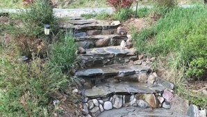Ein steiniger Weg führt einen Hügel hinauf, im Hintergrund ist ein kleines Haus zu sehen.