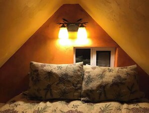 Cozy attic bedroom with a sloped ceiling, featuring a bed with floral bedspread and a wall-mounted light fixture.