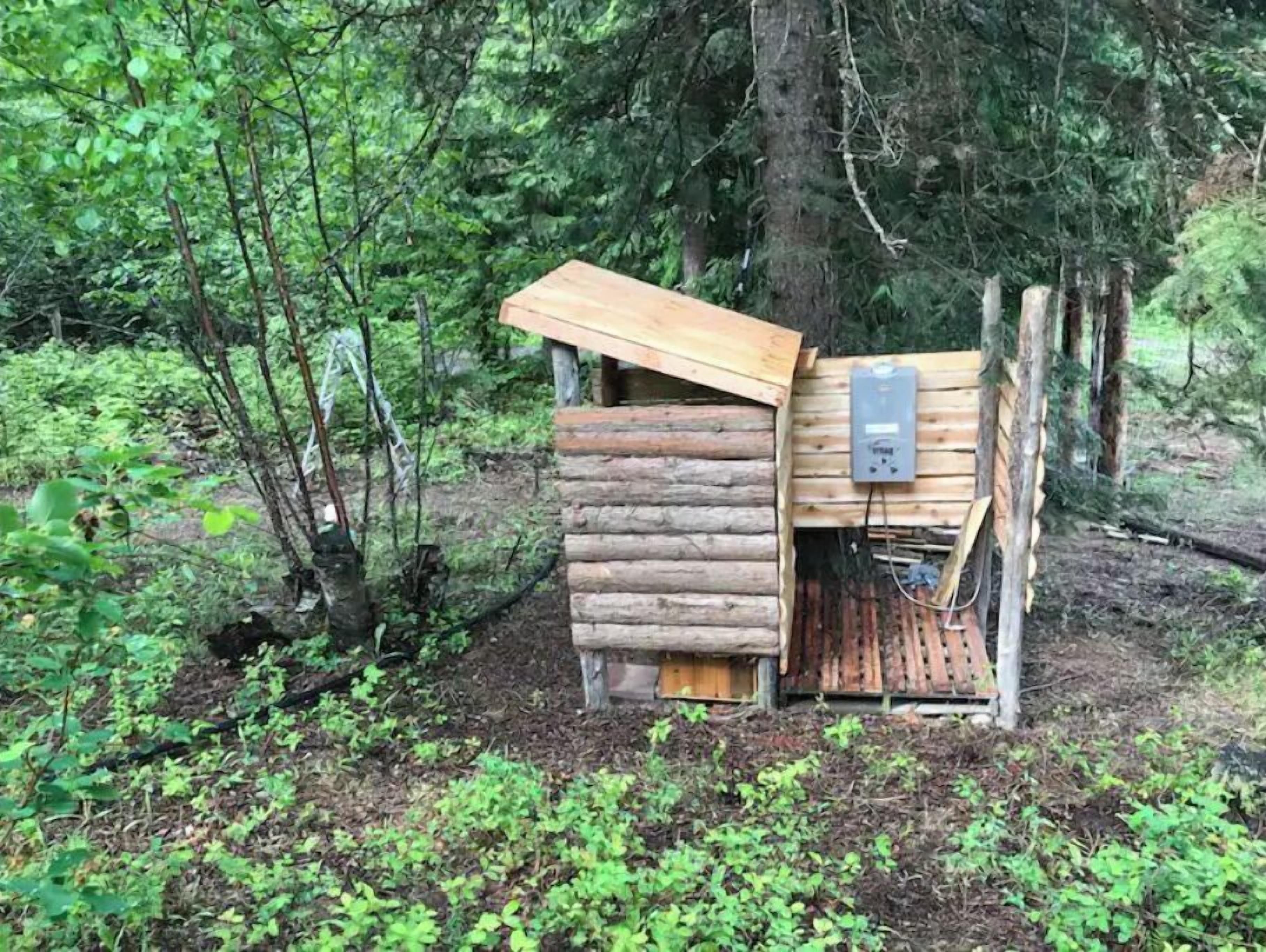 A rustic wooden cabin with a slanted roof, surrounded by dense forest.