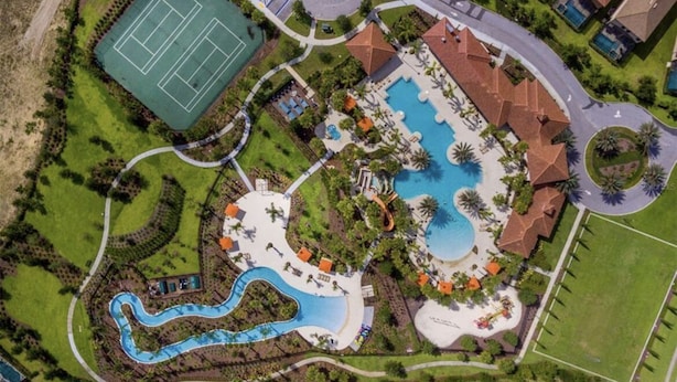 An aerial view of a resort with a swimming pool, tennis court, and landscaped areas.