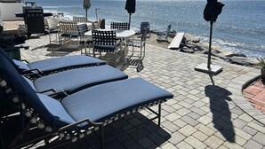 Eine Strandlounge mit Liegestühlen, Sonnenschirmen und einem Grill.