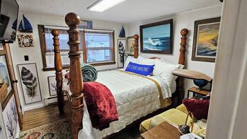 A bedroom with a four-poster bed, a window with blinds, a painting of a seascape, and a framed picture on the wall.
