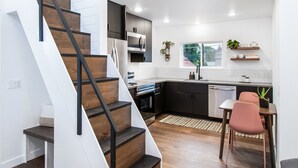 A modern kitchen with dark cabinets, a white countertop, and a dining area with a table and chairs. - Private guest house, king bed, work-from-home friendly, fully equipped kitchen (Denver)