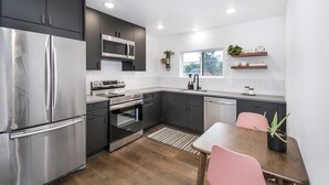 A modern kitchen with stainless steel appliances, dark cabinetry, and a wooden dining table. - Private guest house, king bed, work-from-home friendly, fully equipped kitchen (Denver)