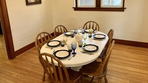 A dining room with a round table set for six, wooden chairs, a chandelier, and a window with a view of a building. - Charming & convenient house in downtown Marshall (Marshall)