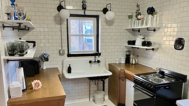 A compact kitchen with white tiled walls, a window, a sink, a stove, and various kitchen items on shelves. - Charming & convenient house in downtown Marshall (Marshall)