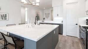 Une cuisine moderne dotée d’un grand îlot central, de meubles blancs et d’une cuisinière à gaz.