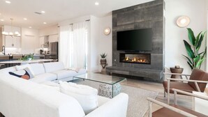Un salon moderne avec une cheminée, un téléviseur à écran plat, un canapé et, au fond, un coin repas.