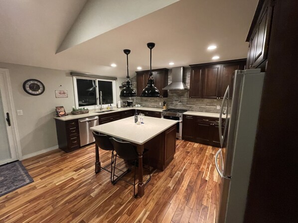 A modern kitchen with wooden flooring, a central island, dark wooden cabinets, and stainless steel appliances.