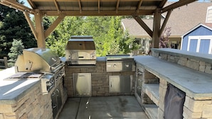 An outdoor kitchen with a stone countertop, a grill, and a built-in sink. - Willow Creek Oasis with Amazing Outdoor Kitchen (Centennial)